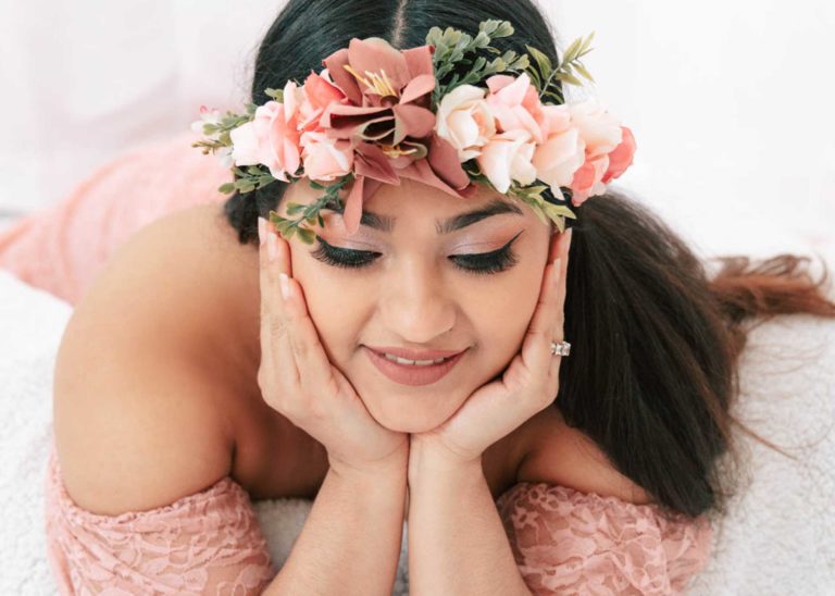 featured Smiling pregnant mother laying on the floor with a flower headband looking away
