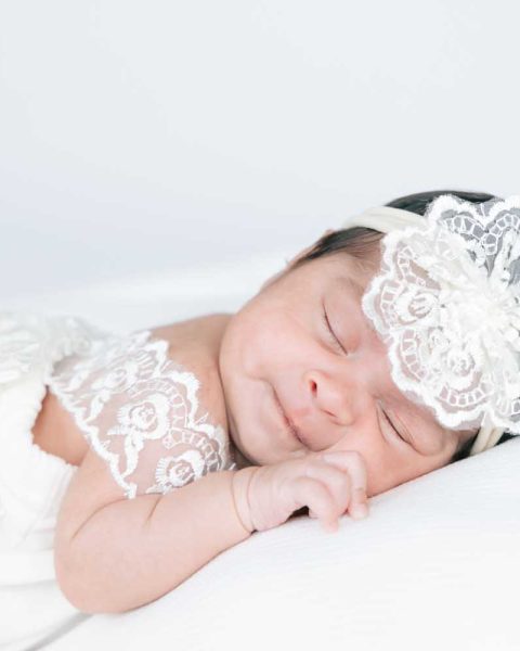 sleeping newborn girl in a white dress and flower head band