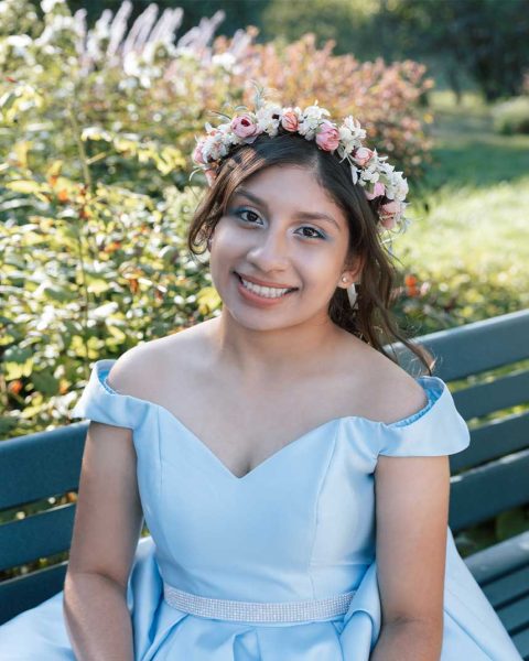 Smiling teenager with a princess dress on a bench surrounded by flowers.